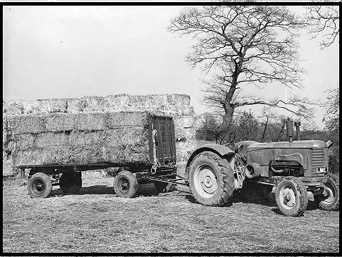 A Massey Harris Tractor pulling a trailer loaded with bales.